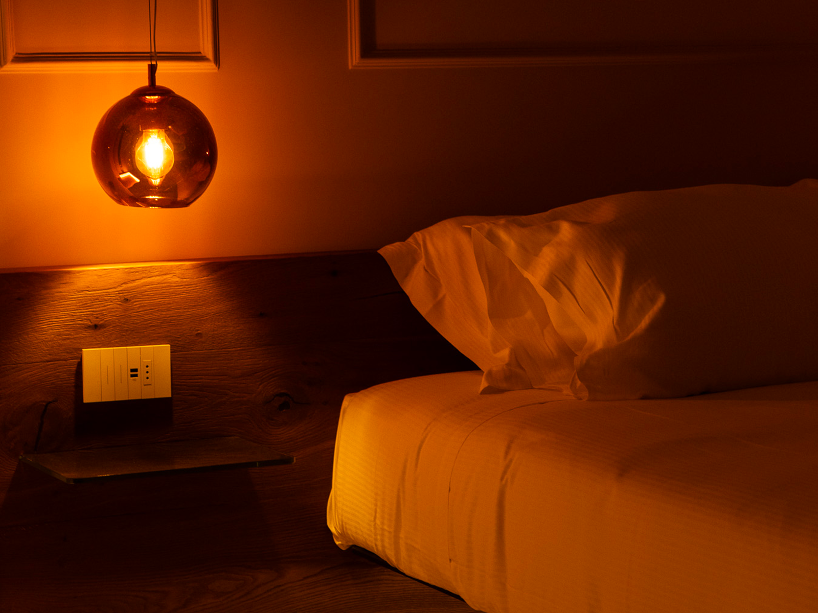 Elegancia Sofisticada en el Dormitorio Lámpara cálida sobre mesita de noche de madera junto a la cama.